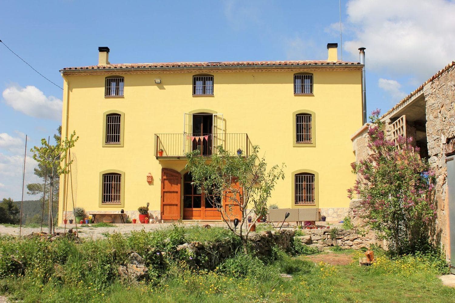 Fachada amarilla de la masía de La Llacuna bajo un cielo azul