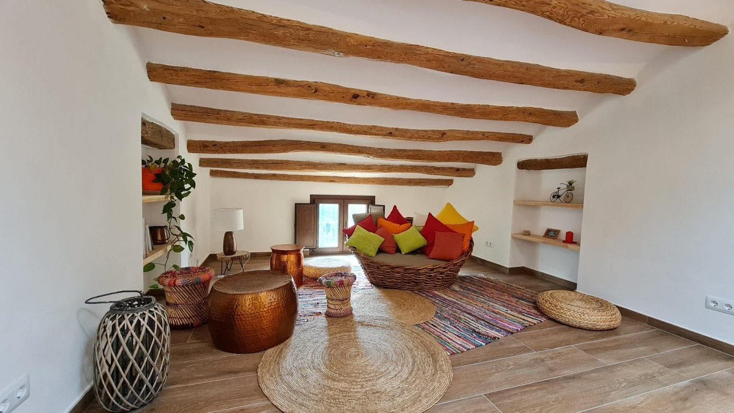 Salón de la masía con vigas de madera vistas y sofá de mimbre
